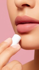 Naklejka premium A close-up of a person applying lip balm, showcasing soft lips against a pink background