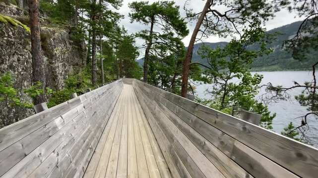 Hamaren Activity Park wooden walkway POV camera view 4K footage. Walking along Fyresvatnet lake surraunded pine trees forest during late summer windy day. Traveling and beauty of Scandinavia concept.