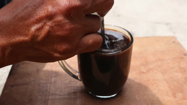the right hand of a Javanese man is stirring a cup of coffee with a small spoon