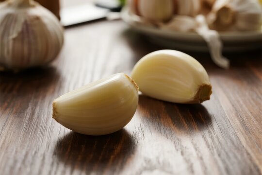 Close-up of garlic cloves on a wooden surface with a bulb in the background