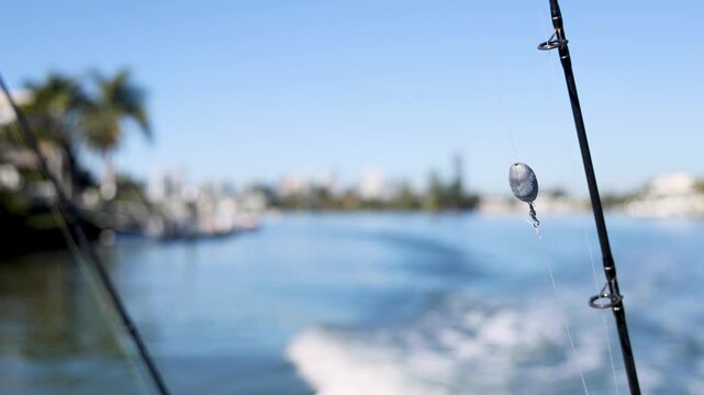 A close-up shot of a fishing rod and line with a fishing sinker and hook attached, on a moving boat, with a tropical resort and blue sky in the background.