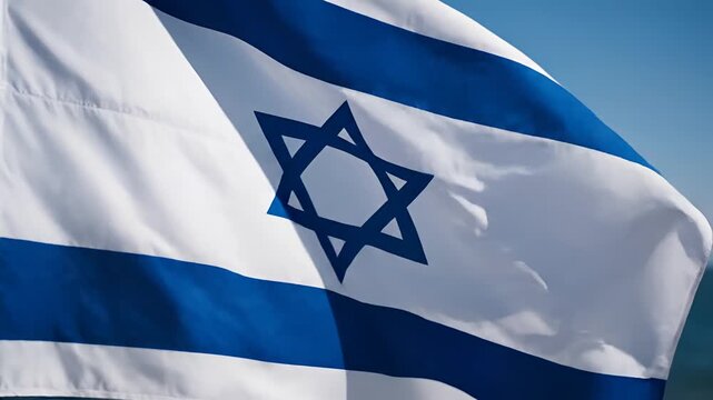 Closeup of the Israeli flag waving in the wind against a blue sky.
