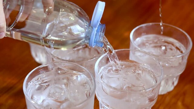 Pouring Fresh Water From Plastic Bottle Into Glass Cups With Ice