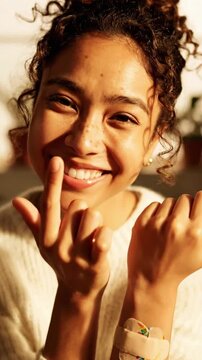 Bicultural woman touches a bandage on her arm in a bright room with plants and soft light