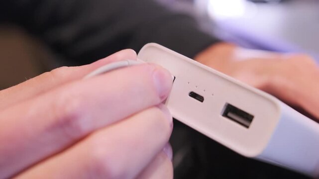 Close-up of hand inserting USB cable into power bank port for charging mobile devices, portable energy supply connection on workspace desk. Female hand Inserting USB cable into power bank