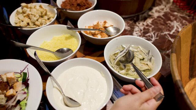 Person Serving Anchovies and Caesar Salad Toppings at International Buffet