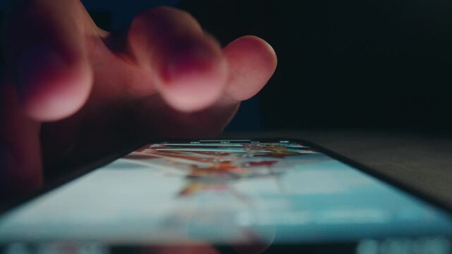 Mobile phone news scrolling at night. Macro view shows male hand browsing social feed on bright screen. Mobile phone use illustrates digital habits constant news checking and online media consumption.