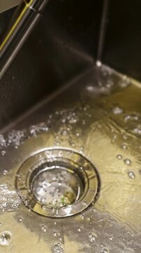 Water Running from a Faucet into a Stainless Steel Kitchen Sink Drain