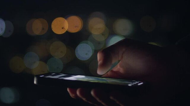 Male hand scrolling smartphone screen at night with city lights background. Mobile communication concept shows digital connection social media messaging online interaction and modern smartphone use.