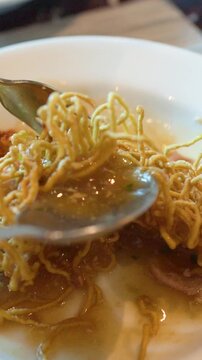 Close Up of Person Eating Crispy Thai Noodles with Pork and Spicy Soup