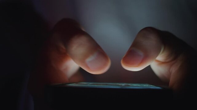 Smartphone in male hands with close up fingers tapping touchscreen while scrolling social media in dark mood. Smartphone use shows digital lifestyle online communication and modern mobile technology