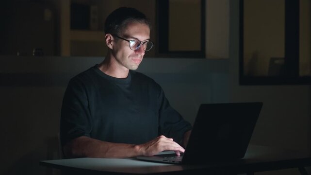 Freelancer working on laptop at night, typing with calm concentration in dark room. Digital nomad lifestyle shows independence, online income, flexible work and modern freelance career