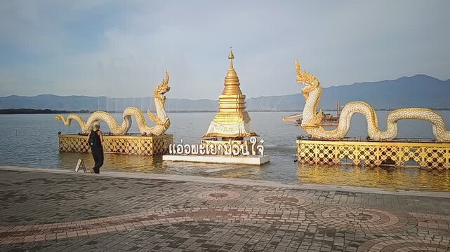 A traveler photographing the iconic Naga sculptures and Buddhist stupa at the waterfront of Kwan Phayao, Northern Thailand.