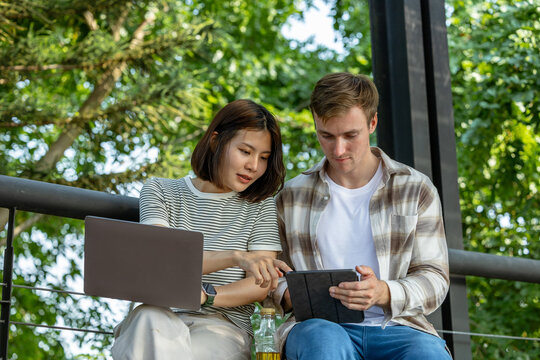 Man and woman working together on a tablet outdoors.