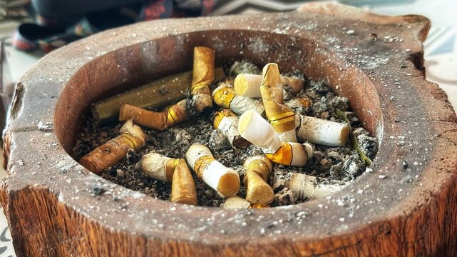 A close-up view of many cigarette butts in a wooden ashtray on a table indoors.