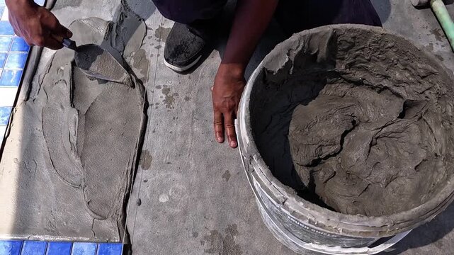 Worker applying wet cement mortar on swimming pool floor for tiling