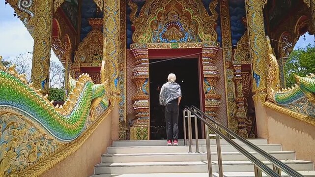 Tourist entering an intricately decorated traditional Thai temple adorned with Naga sculptures.