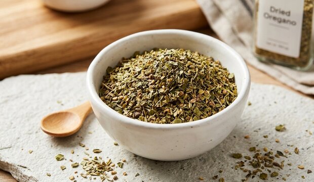 Dried oregano flakes in a white ceramic bowl with wooden spoon on stone plate, aromatic Mediterranean herb for pizza, pasta, and Italian cooking.