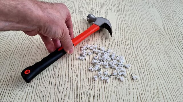 Claw hammer with red handle rests on light wooden surface beside scattered white plastic cable clamps, highlighting everyday repair tools and hardware in a practical close up view