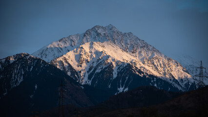 Obraz premium Majestic Winter Alpine Landscape at Sunset with Pine Trees, Sun-Kissed Snow Ridges Above Dark Mountain Woods