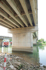 Fototapeta premium Concrete bridge pier extending over a river with lush green banks and vegetation, illustrating infrastructure and natural beauty merging seamlessly.