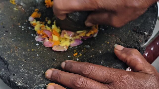 Close-up of a person crushing and grinding shallots and garlic using a traditional stone mortar and pestle (cobek)