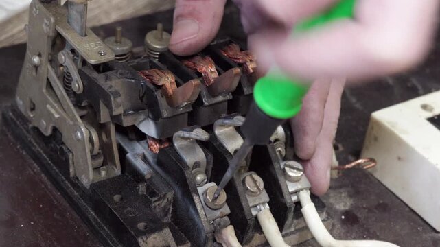 Electrician repairing an old industrial contactor with a screwdriver, hands of electrician unscrew screws on terminals, Professional electrical work.