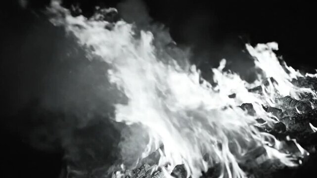 Black and white close up of a roaring fire burning wood in a pile with smoke and flames