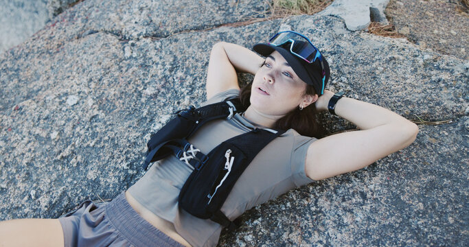 Tired, woman and relax for fitness on rocks from exercise, intense training and recovery. Thinking, female person or exhausted with fatigue, athlete burnout and break in nature from challenge