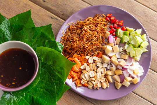 Traditional Thai miang kham ingredients on plate with betel leaves lime chili peanuts coconut sauce ready for wrapping fresh herbs savory sweet street snack