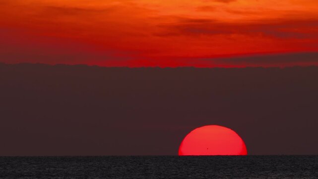 Cinematic sunset with a fiery red sun disappearing beyond the ocean horizon. Vibrant coastal landscape at twilight, ideal for vacation, wanderlust, and serene seascape concepts.
