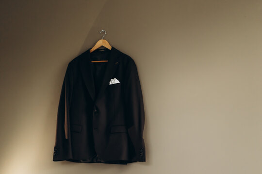 Stylish dark suit jacket hanging on wall