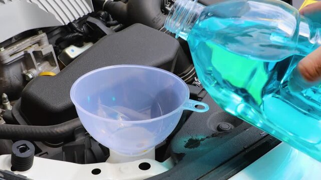自動車のボンネットを開けてウィンドウォッシャー液を補充している