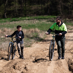 Obraz premium Father and son enjoy a bike ride on a sunny day, along a sandy trail.