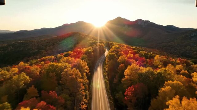Flying over a winding road with the sun rising behind the mountains in autumn