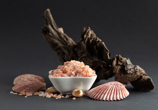 Pink himalayan salt with snags and seashells on a black background.