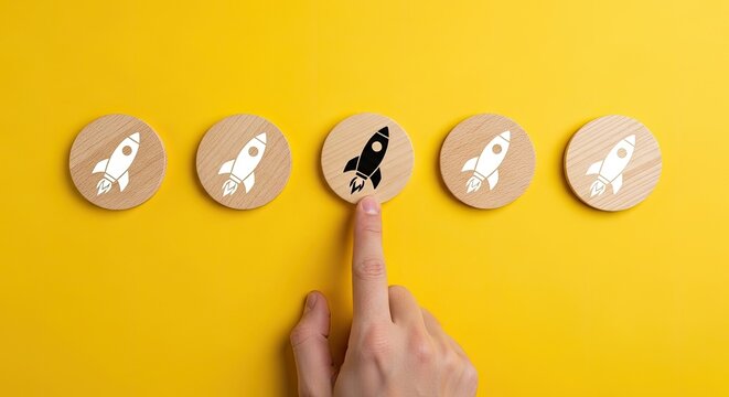 A single human index finger points to a distinct black rocket icon among identical white rocket icons placed on wooden circular discs against a vibrant yellow background.