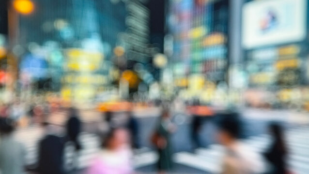A blurred image of a busy urban intersection, filled with people and vibrant city lights showcasing the hustle and bustle of city life.