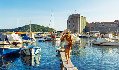 Obraz premium female traveler with straw hat looking at old port and fort st ivan in Dubrovnik. Travel destination, tour tourism in Croatia