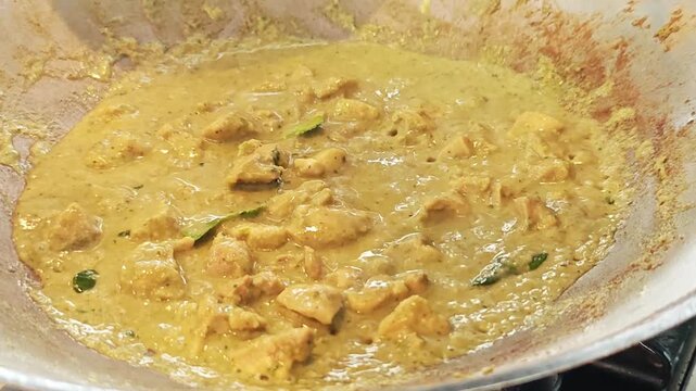 Pouring fresh coconut milk into a bubbling Thai green curry in a wok.