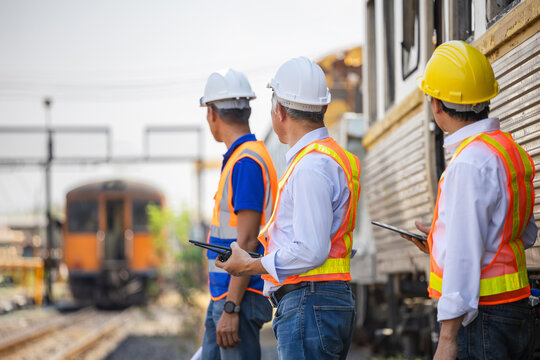 Group of railway engineers in safety vests using walkie-talkie and tablet for train inspection, Team of professional inspectors monitoring train operations and railway infrastructure at the station