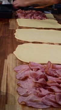 Vertical close up of a hand making pan de jamon with ham on wood table
