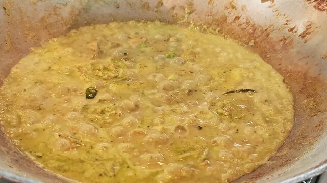 Close-up of bubbling Thai green curry simmering in a large wok.