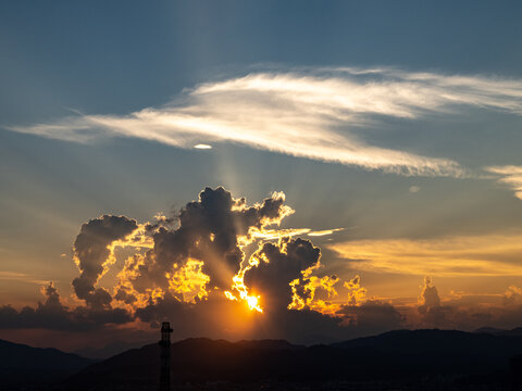 黄色い夕焼けに立ち上がる怪物の様なシルエットの雲と光の筋