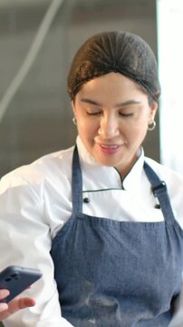 Vertical video: Coworker presenting phone, chef glancing, reading and laughing in kitchen in apron