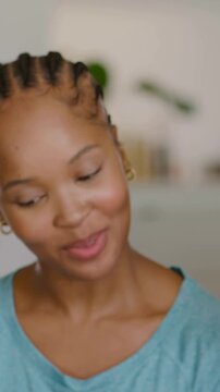 Vertical video: Laughing woman softly smiling after offscreen remark on couch at home, in teal tee