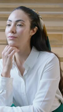 Vertical video: Camera tightening woman with scarf supporting chin thinking shifting gaze on stairs