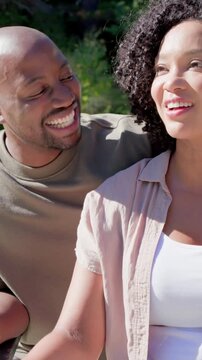 Vertical video: Talking man making woman laugh then both resting head on bench in park, olive tee