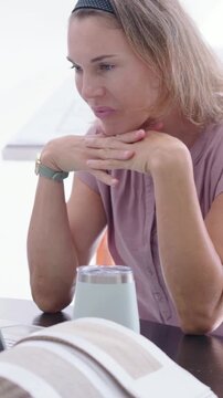 Vertical video: Typing woman in pink top pausing, smiling, working at home with laptop and tumbler