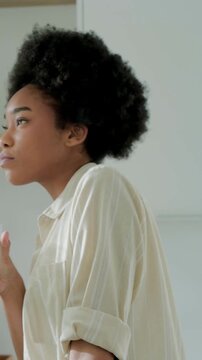 Vertical video: Hand lifting glass, Black woman sipping water at kitchen, wearing light shirt